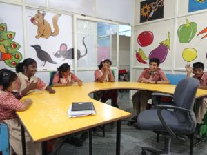 Volontaire de Globalong en Inde avec des enfants en salle de classe, engagés dans des activités éducatives autour d'une table jaune avec des décorations murales colorées