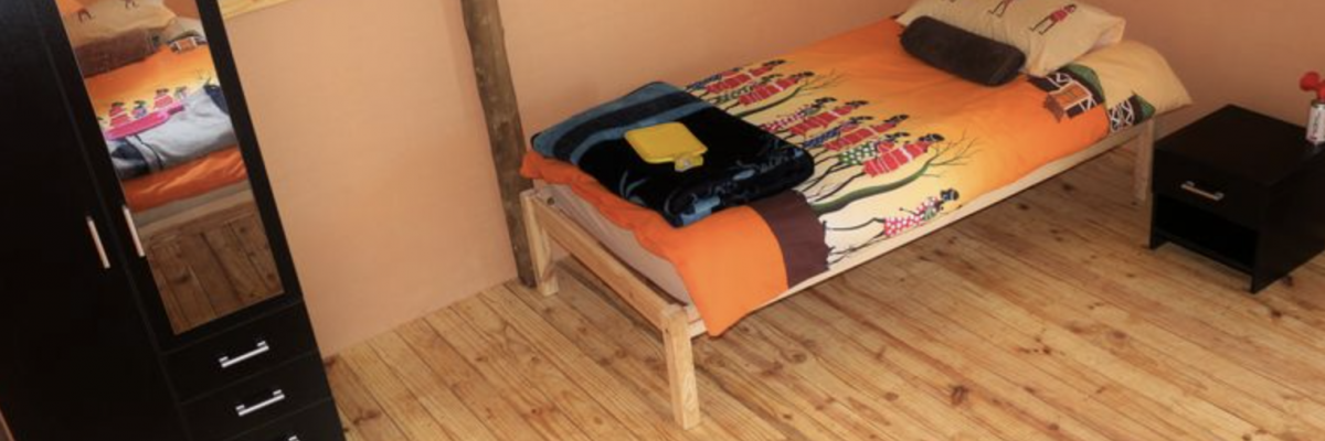 Chambre simple en tente aménagée pour les volontaires en Namibie, avec lit individuel, armoire et décoration colorée, dans le cadre d’un projet humanitaire Globalong.