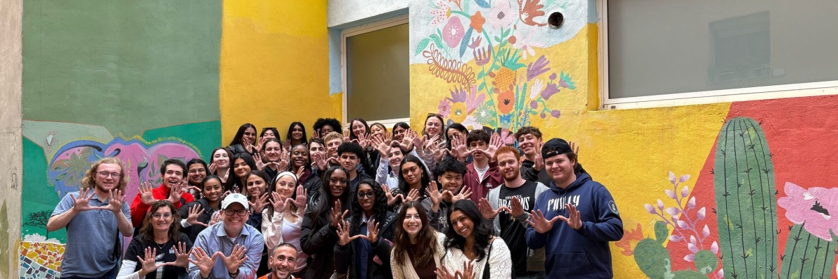 Jeunes bénévoles Globalong devant une fresque murale colorée lors d'un projet communautaire Groupe de jeunes bénévoles participant à un projet communautaire avec Globalong, posant devant un mur coloré peint de fleurs et de cactus.