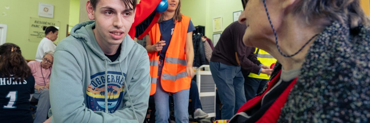 Échange entre un jeune bénévole et une personne âgée lors d'une activité en résidence Un jeune bénévole échange avec une personne âgée dans une résidence, lors d'une activité intergénérationnelle animée par des volontaires.