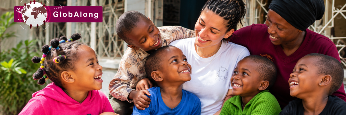 Bénévole et membre de l'équipe locale entourées d'enfants devant un bâtiment