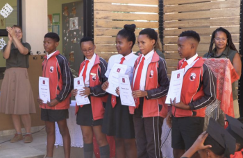 Cinq élèves San en uniforme reçoivent leurs certificats lors d’une cérémonie de fin d’année à l’école communautaire en Namibie, entourés de leurs enseignants.