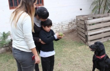 Un enfant participant à une séance de thérapie canine, aidé par deux adultes, avec un chien noir attentif en arrière-plan, dans le cadre d'un programme Globalong.