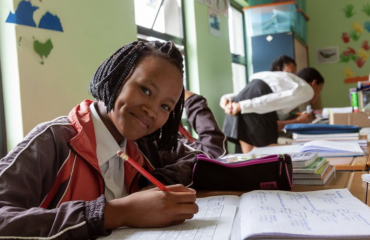 Élève San souriante écrivant dans son cahier pendant un cours à l’école communautaire en Namibie, dans le cadre d’un projet éducatif Globalong.
