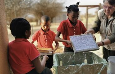 Enfants San participant à un atelier éducatif en plein air en Namibie avec une volontaire Globalong, apprenant à recycler et à fabriquer du papier artisanal.