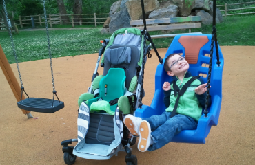 enfant en situation de polyhandicap souriant sur une balançoire adaptée dans un parc inclusif
