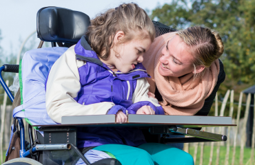 bénévole échangeant un regard complice avec une enfant polyhandicapée en fauteuil roulant