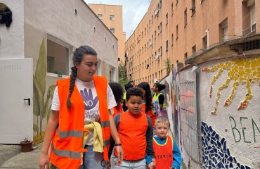 Une jeune bénévole encadre deux enfants lors d'une activité communautaire organisée par Globalong, dans une cour ornée de fresques murales colorées.